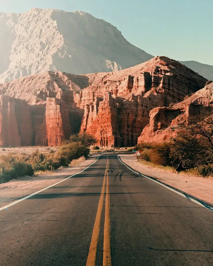 Estrada asfaltada cortando formações de rocha vermelha, como na Ruta 68 entre Salta e Cafayate