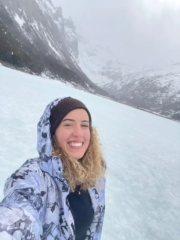 Sarah sorrindo na neve, com montanhas ao fundo